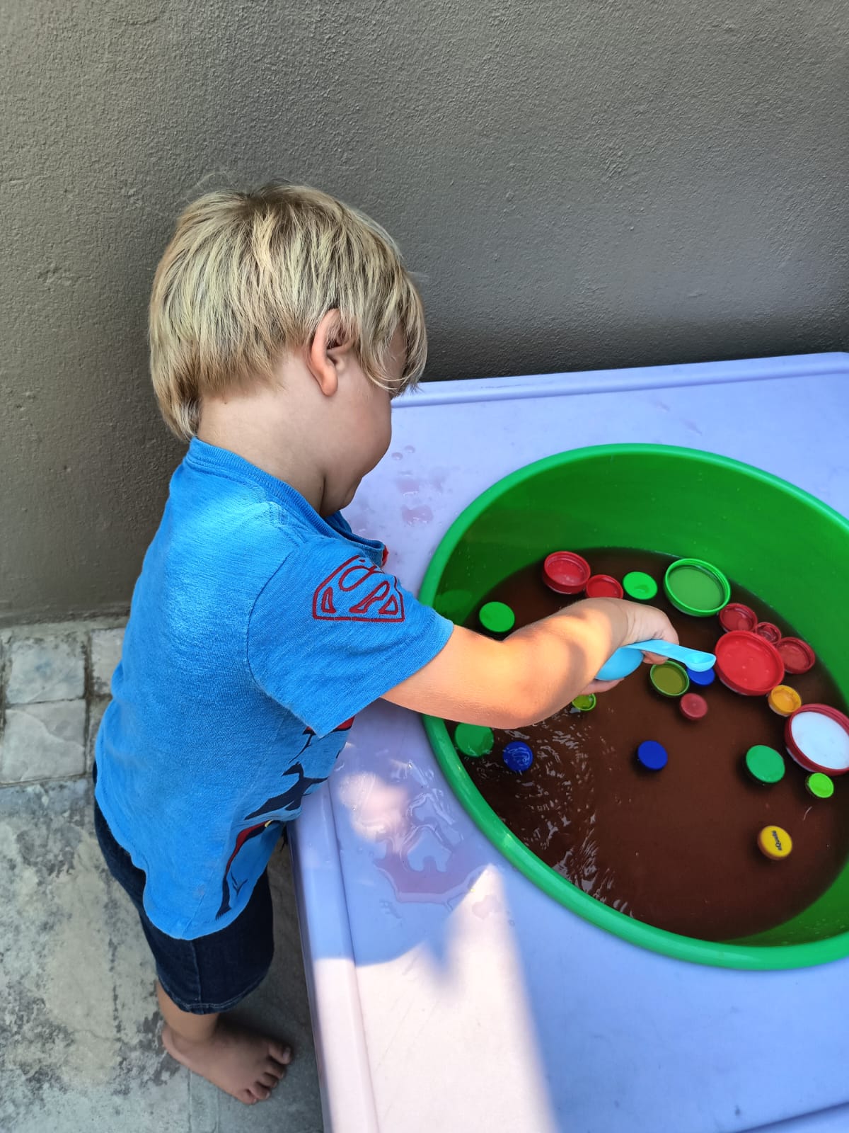 A toddler exploring a sensory bin of coloured lids and water