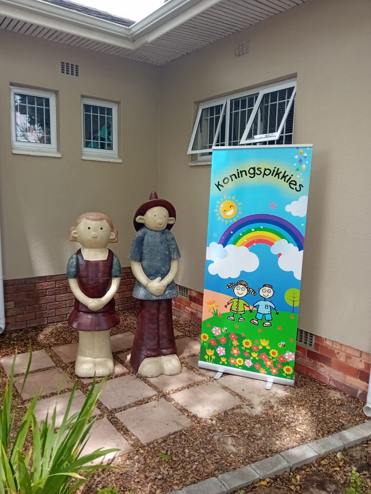 The Koningspikkies Zambezi entrance with wooden child statues and the rainbow banner